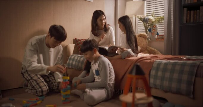 딸과 함께 동화책을 읽는 엄마와 아들과 함께 블록을 쌓아 타워를 만드는 아빠, 줌아웃 돌리 와이드 샷
