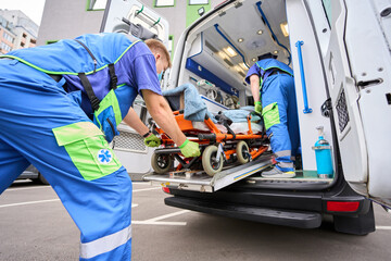 Paramedic in a protective mask unloads a patient from an ambulance - obrazy, fototapety, plakaty
