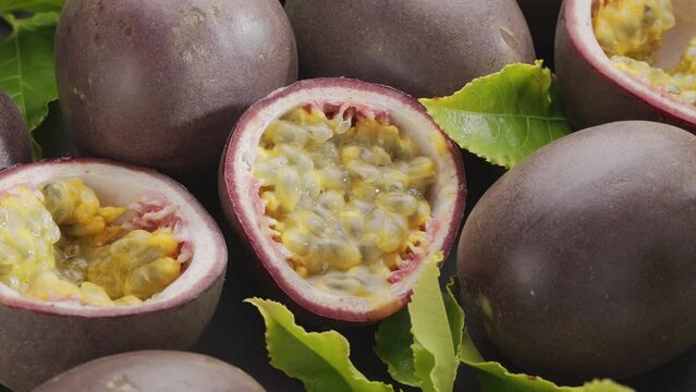 Ripe passion fruits with passion fruit seeds and passionfruit leaves slowly move in the frame on a gray stone table. Nice exotic fruit background for your projects. Macro video shooting.