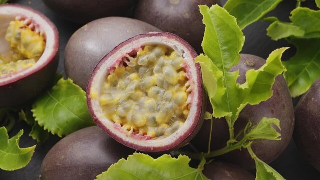 Ripe passion fruits with passion fruit seeds and passionfruit leaves slowly move in the frame on a gray stone table. Nice exotic fruit background for your projects. Macro video shooting.