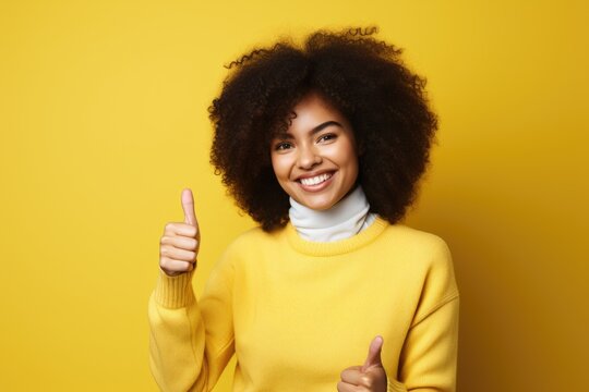 A woman wearing a yellow sweater is seen giving a thumbs up gesture. This image can be used to convey approval, success, positivity, or endorsement in various contexts.