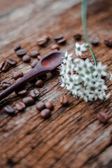 Colher de pau com grãos de café torrado espalhados e pequenas flores desfocadas 