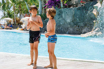 Two happy little kids boys jumping in the pool and having fun on family vacations in a hotel...