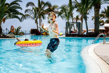 Happy little kid boy jumping in the pool and having fun on family vacations in a hotel resort. Healthy child playing in water.