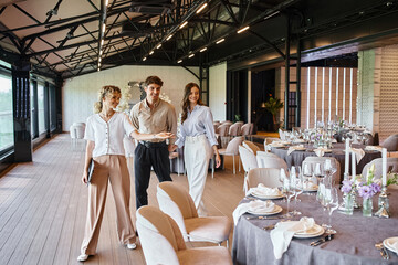 event manager showing festive tables to happy couple in love in event hall with wedding decor