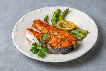 Grilled, baked salmon served on a plate with asparagus and potatoes.