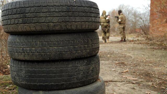 Close-up of car tires, two soldiers in camouflage uniforms and weapons are standing in the background. The location of the army in the autumn forest.