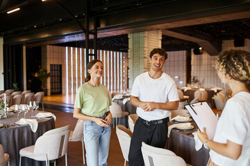 smiling decorators talking to team lead near festive tables in modern decorated banquet hall