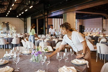 banquet decorator arranging table setting near colleagues working in event hall, creative team