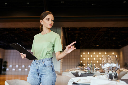 event coordinator with clipboard pointing with pen at table with festive setting in banquet hall