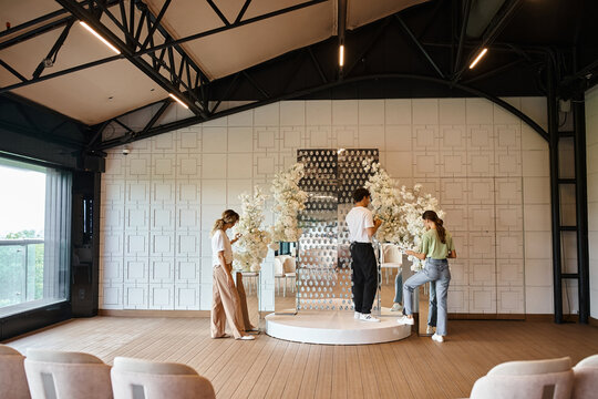 group of decorators decorating modern event hall with white flowers, teamwork and event preparation - Powered by Adobe
