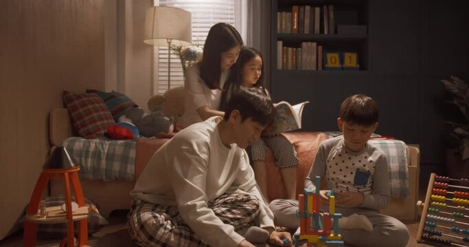 집에서 책을 보고 장난감을 쌓다가 미소 지으며 카메라를 보는 행복한 가족