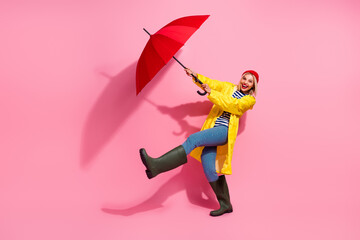 Full length photo of pretty excited woman dressed rain coat walking under parasol air blowing empty...