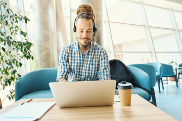 Young IT specialist settled down with laptop under a ficus