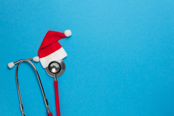 Medical red stethoscope with christmas hat on blue background. Christmas and New Year concept. Creative medical winter greeting card. Top view, flat lay, copy space