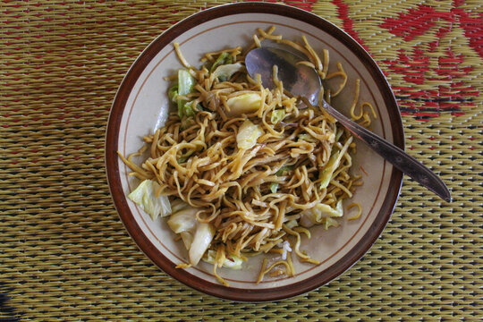 Traditional javanese fried noodle on a plate with spoon, with tikar as background, flat lay or top view
