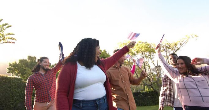 Happy diverse male and female friends dancing with flags in sunny garden