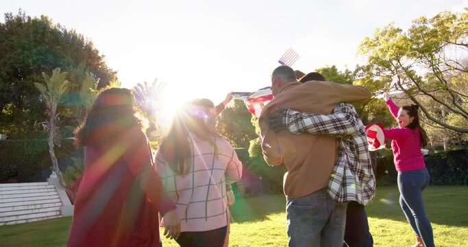 Happy diverse male and female friends dancing with flags in sunny garden
