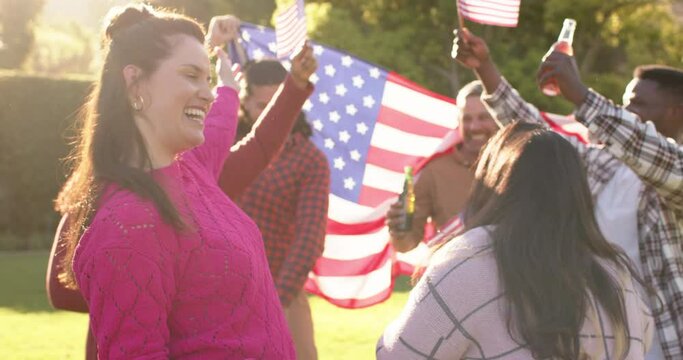 Happy diverse male and female friends dancing with flags in sunny garden