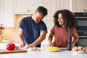 Couple At Home With Man With Down Syndrome And Woman Rolling Dough For Pizza In Kitchen Together