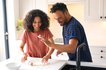 Couple At Home With Man With Down Syndrome And Woman Rolling Dough For Pizza In Kitchen Together