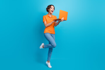 Full length photo of impressed crazy woman wear orange t-shirt jeans pants astonished staring at laptop isolated on blue color background