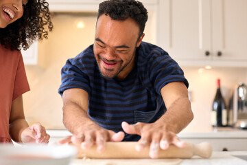 Couple At Home With Man With Down Syndrome And Woman Rolling Dough For Pizza In Kitchen Together