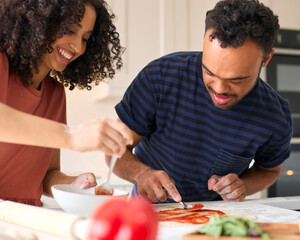Couple At Home With Man With Down Syndrome And Woman Putting Sauce On Pizza In Kitchen Together