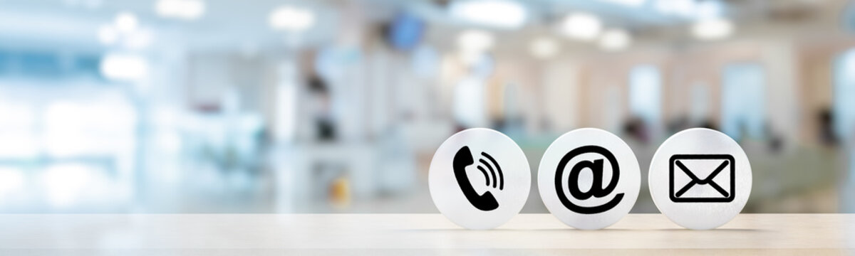 Contact Us. telephone, envelope letter and e-mail symbols on Wooden round in row on table with blurred office background, contact us symbols or web banner