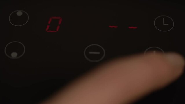 Close up of woman finger turning on glass-ceramic kitchen stove. Person includes an electric stove. Modern technology. Touch panel of induction cooker. Girl select function on Induction stove.