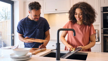 Couple At Home With Man With Down Syndrome And Woman Clearing Up And Washing Dishes After Meal