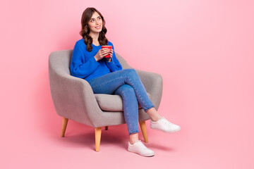 Full body portrait of cute creative lady sit soft cozy chair hold fresh coffee cup look empty space isolated on pink color background