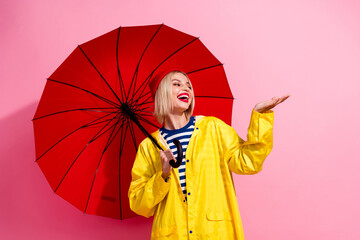 Photo of sweet impressed woman dressed rain coat holding parasol arm empty space isolated pink color background © deagreez