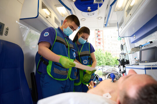 Team of paramedics makes a cardiogram to man in ambulance