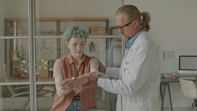 Medium shot of Caucasian teenage girl with disability trying on prosthetic arm while adult male prosthetist helping her