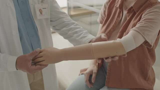 Cropped shot of unrecognizable patient with disability trying on prosthesis on amputated arm, having appointment with professional prosthetist in clinic