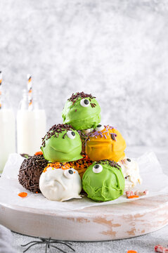 Naklejki Homemade funny monster mini cakes or cake pops in a colored chocolate glaze and sugar sprinkles. Halloween treat on a concrete background.