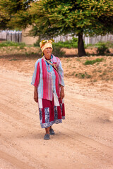 basarwa old african woman walking on a dirt road in the traditional village