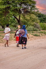 Obraz premium three basarwa african woman strolling on a dirt road to get to the traditional village