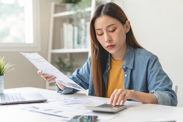 Young Asian woman looking at credit card invoice in her hands and worry about cash on bills payday - obrazy, fototapety, plakaty