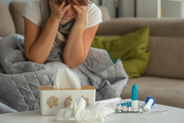 Medicines for colds and paper napkins are on the table, a woman with signs of flu and colds is sitting in the background