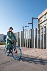 Stylish business woman in green suit and helmet riding her bicycle at the financial district with modern building on the background