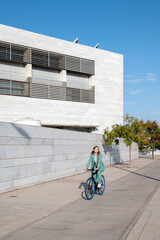 Stylish business woman in green suit riding her bicycle at the financial district with modern building on the background