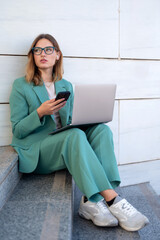 Business woman sitting on stairs outside office building while working with laptop and having a video call