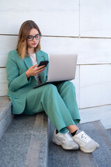 Business woman sitting on stairs outside office building while working with laptop and having a video call