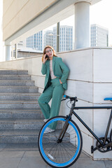 Business woman standing on stairs outside office building while talking on cellphone next to a bike