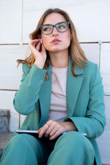 Business woman sitting on stairs outside office building while using her earphones