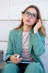 Business woman sitting on stairs outside office building while using her earphones