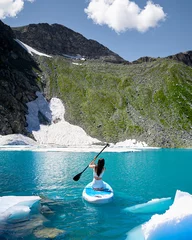 Foto op Plexiglas a woman swims on a SUP surf on a blue mountain lake between glaciers high in the mountains © MikeFrame