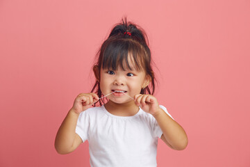 Headshot portrait of little asian girl uses dental floss standing over pink isolated background.